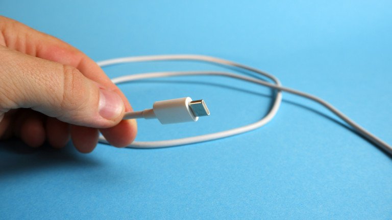 Fingers are holding a white usb cable with a type c interface on a blue background.